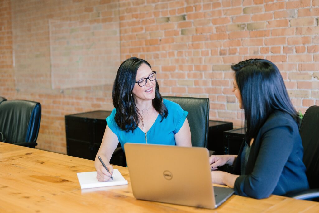 woman in teal t-shirt sitting beside a woman wearing a suit jacket